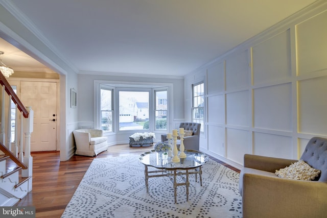 living area with wainscoting, stairs, a decorative wall, crown molding, and dark wood-style floors