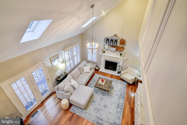 living room with a skylight, high vaulted ceiling, a fireplace with raised hearth, an inviting chandelier, and wood-type flooring