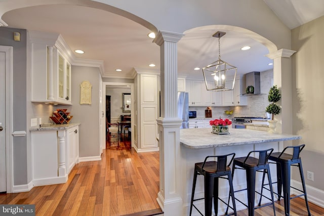 kitchen with appliances with stainless steel finishes, white cabinets, decorative columns, and wall chimney exhaust hood