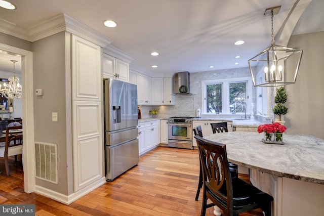 kitchen with an inviting chandelier, wall chimney range hood, visible vents, and appliances with stainless steel finishes