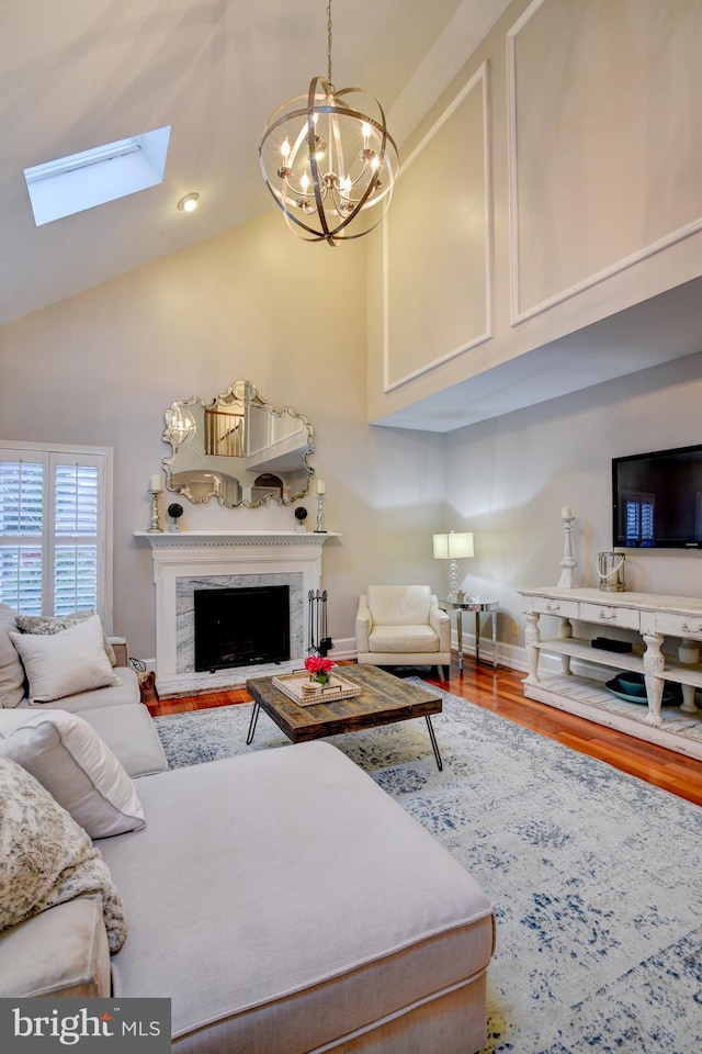 living area featuring an inviting chandelier, wood finished floors, high vaulted ceiling, a skylight, and a premium fireplace