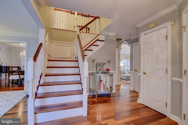 stairway with arched walkways, crown molding, and wood finished floors