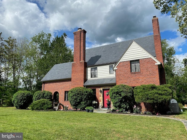 view of front of house featuring a chimney, brick siding, and a front lawn