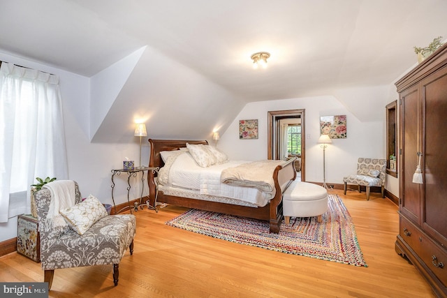 bedroom with vaulted ceiling, light wood-style floors, and baseboards