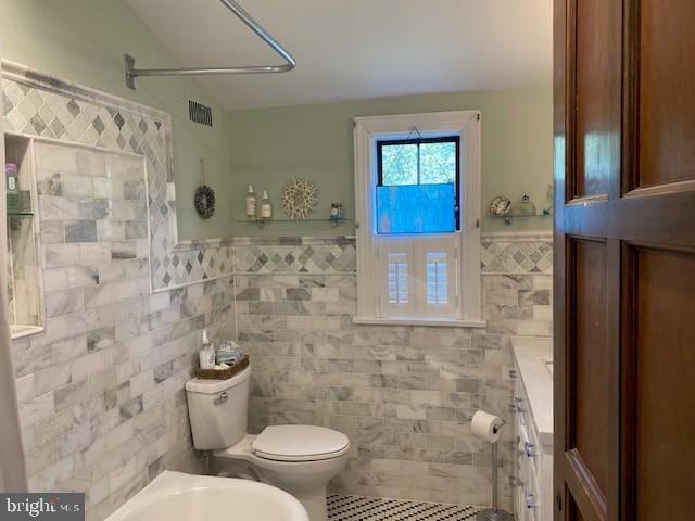 full bathroom with tile patterned flooring, tile walls, toilet, a wainscoted wall, and a bidet