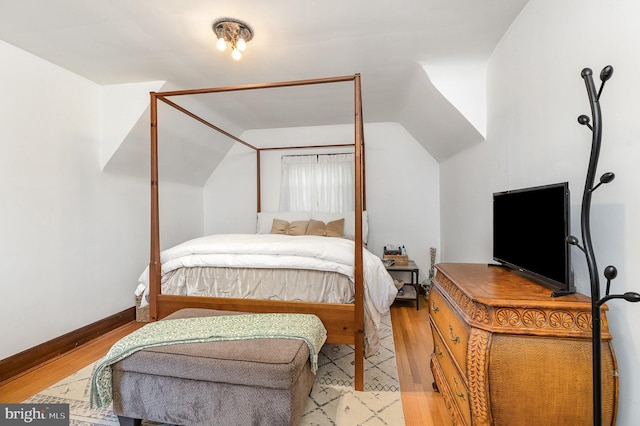 bedroom featuring light wood-type flooring, vaulted ceiling, and baseboards