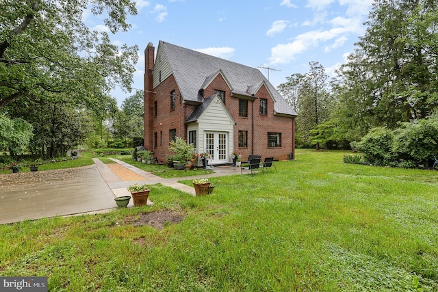 view of side of home featuring french doors, a chimney, a lawn, and brick siding