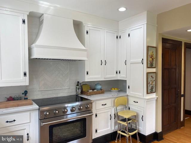kitchen featuring stainless steel range, premium range hood, white cabinetry, and recessed lighting