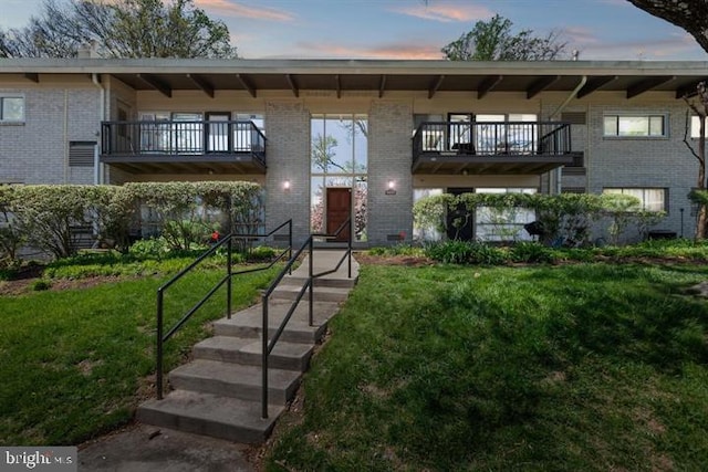 view of property featuring a balcony, brick siding, and a lawn