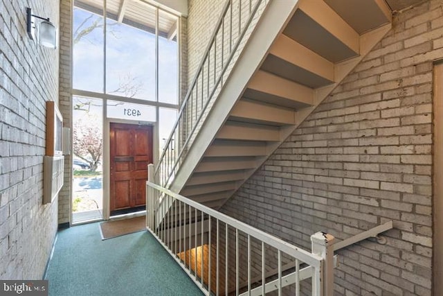 carpeted entrance foyer featuring plenty of natural light, a towering ceiling, brick wall, and expansive windows