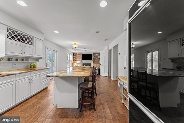kitchen featuring a kitchen breakfast bar, wooden counters, open floor plan, recessed lighting, and dark wood finished floors