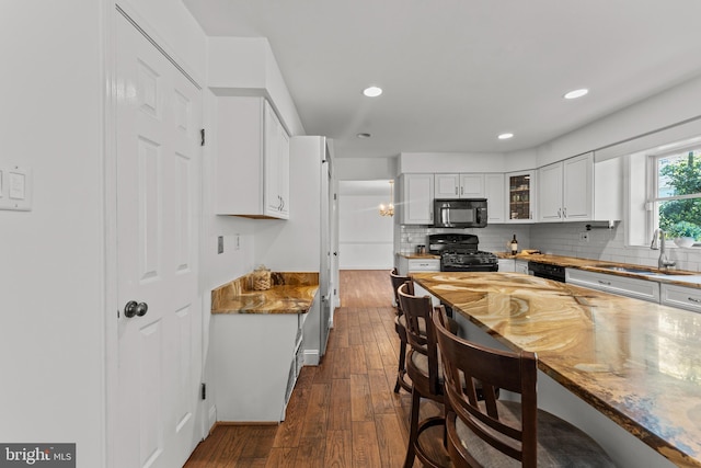 kitchen with a sink, black appliances, a kitchen breakfast bar, dark wood-style floors, and white cabinetry
