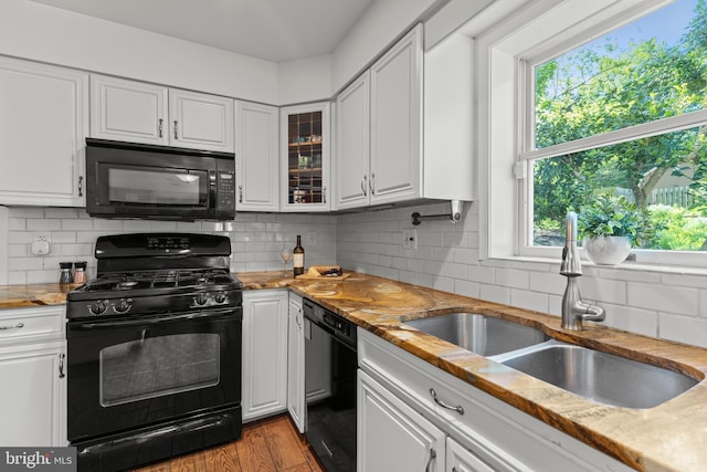 kitchen with black appliances, a sink, white cabinetry, and glass insert cabinets