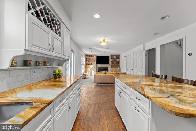 kitchen featuring recessed lighting, white cabinetry, decorative backsplash, a fireplace, and light stone counters