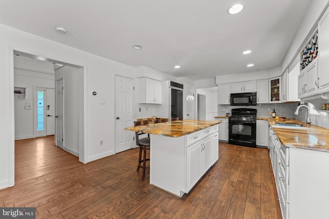 kitchen with black appliances, white cabinetry, a kitchen bar, light stone counters, and a center island