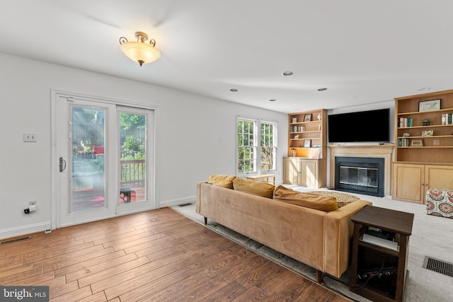 living room featuring a glass covered fireplace, wood finished floors, baseboards, and recessed lighting