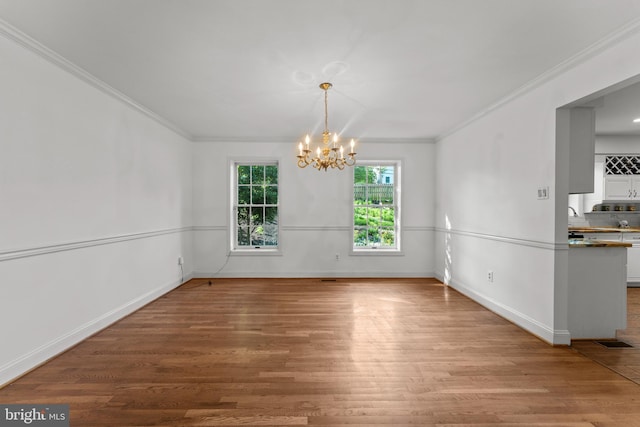 unfurnished dining area with wood finished floors, a chandelier, ornamental molding, baseboards, and a sink