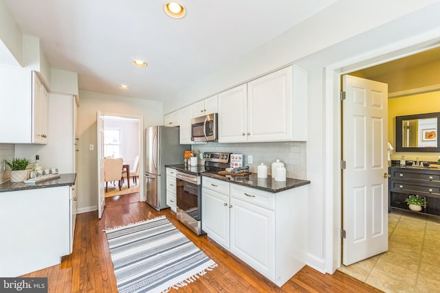 kitchen with appliances with stainless steel finishes, white cabinetry, tasteful backsplash, wood finished floors, and recessed lighting