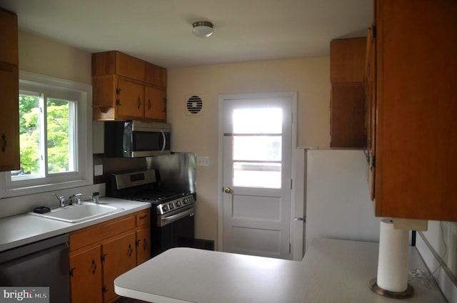 kitchen featuring stainless steel appliances, a sink, light countertops, a peninsula, and brown cabinets