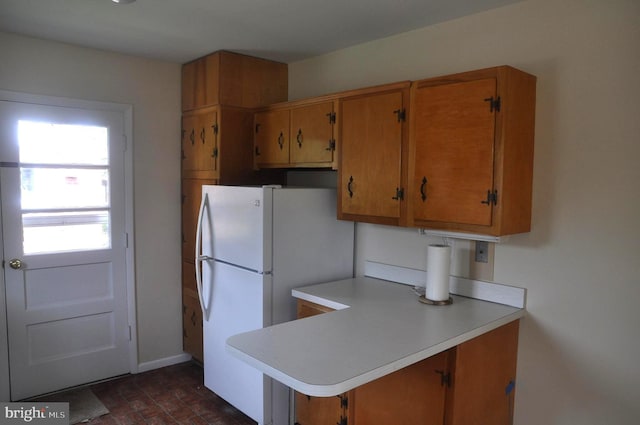 kitchen featuring light countertops, freestanding refrigerator, brown cabinets, baseboards, and a peninsula