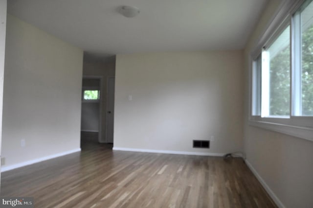empty room with healthy amount of natural light, wood finished floors, and baseboards