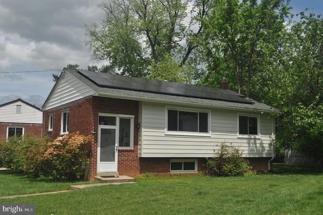 view of front of home featuring a front yard, solar panels, a chimney, and brick siding
