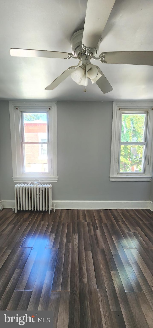 unfurnished room with radiator, plenty of natural light, wood finished floors, and a ceiling fan