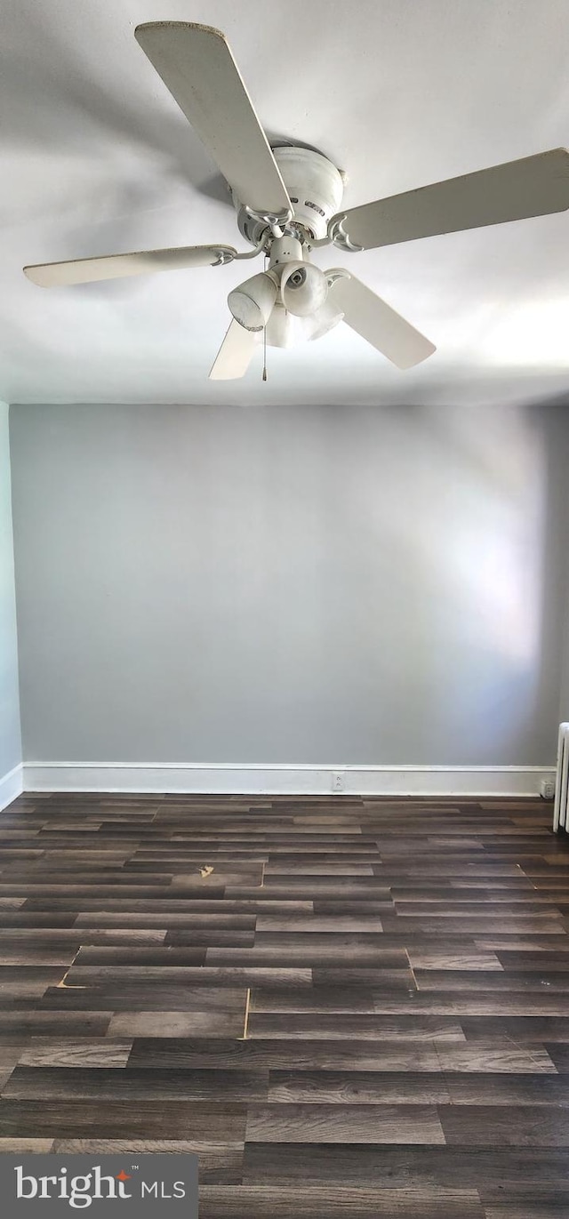 empty room featuring a ceiling fan, baseboards, dark wood finished floors, and radiator