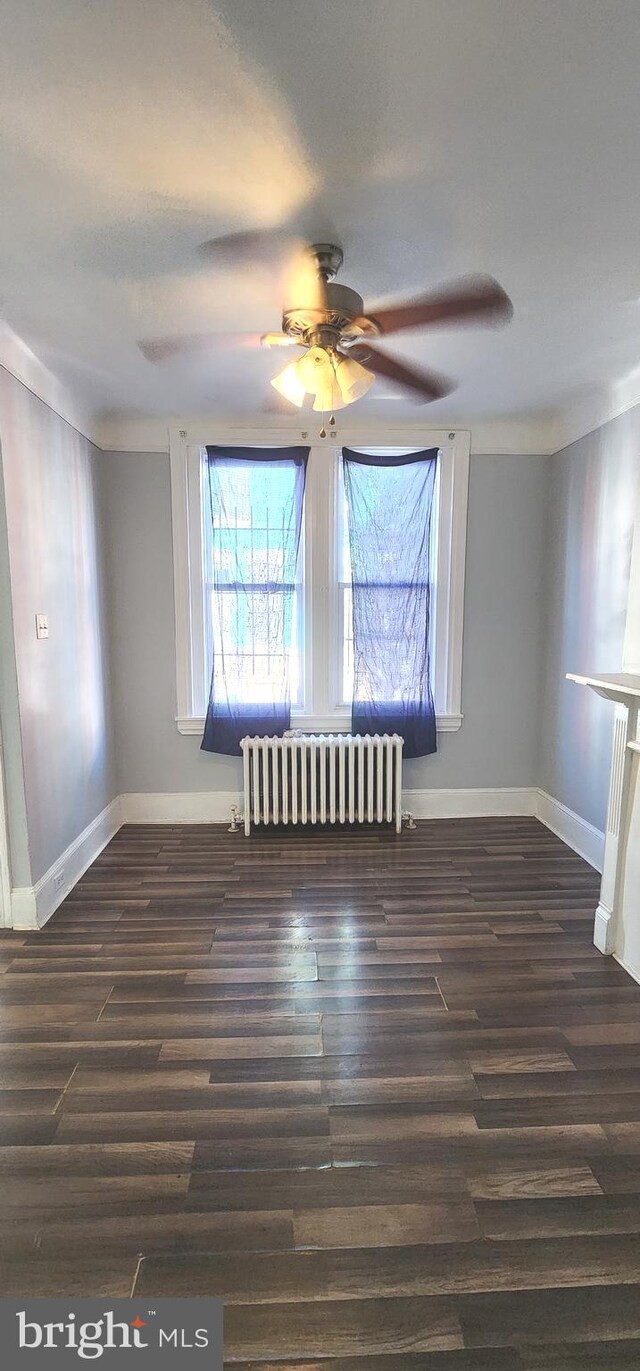 unfurnished room featuring radiator heating unit, ceiling fan, baseboards, and wood finished floors