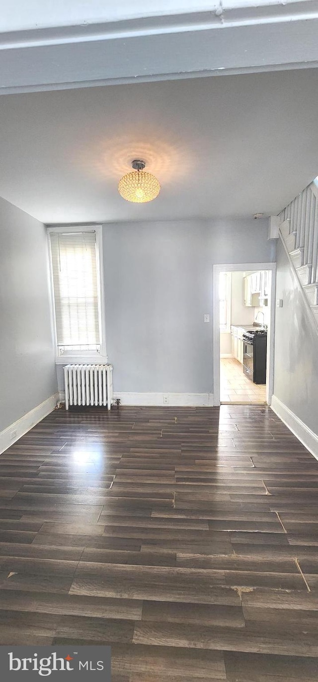 spare room with radiator heating unit, stairway, wood finished floors, and baseboards