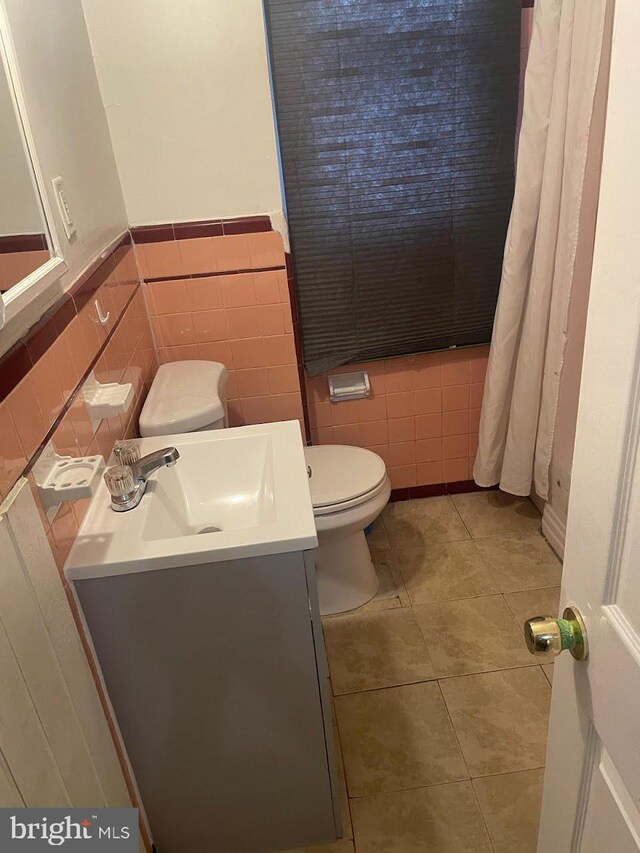 bathroom featuring tile walls, toilet, tile patterned flooring, and wainscoting