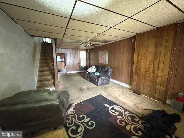 basement featuring stairway, a paneled ceiling, wooden walls, and ceiling fan