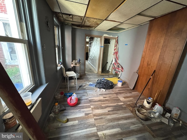 corridor featuring wood finished floors, baseboards, and a paneled ceiling