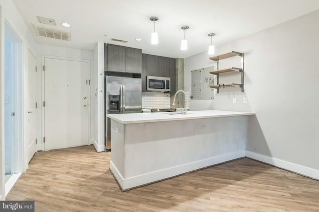 kitchen with a peninsula, a sink, stainless steel appliances, visible vents, and tasteful backsplash