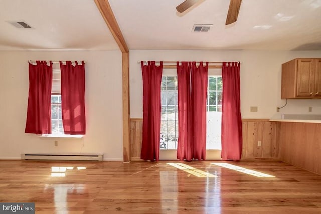 unfurnished dining area with baseboard heating, wood finished floors, wainscoting, ceiling fan, and wooden walls