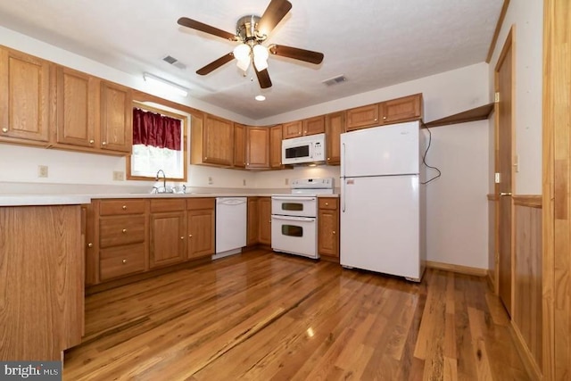 kitchen with white appliances, a sink, a ceiling fan, light wood finished floors, and brown cabinets