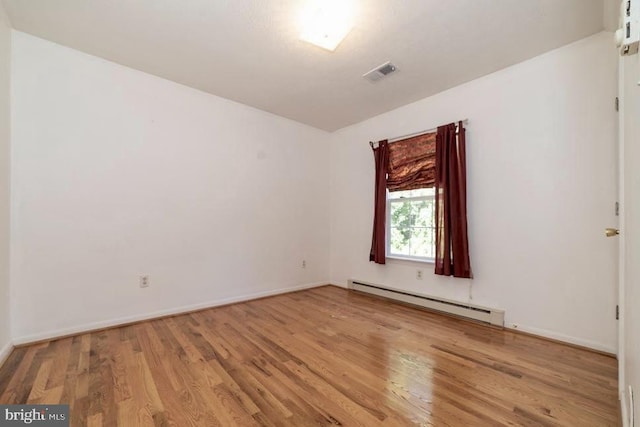 empty room with a baseboard heating unit, wood finished floors, and baseboards