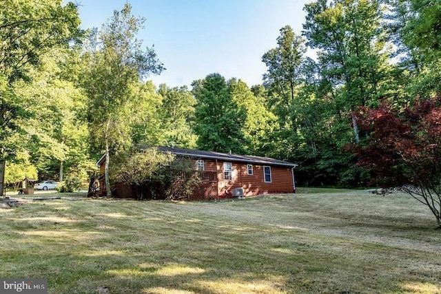 view of grassy yard featuring a view of trees and a deck
