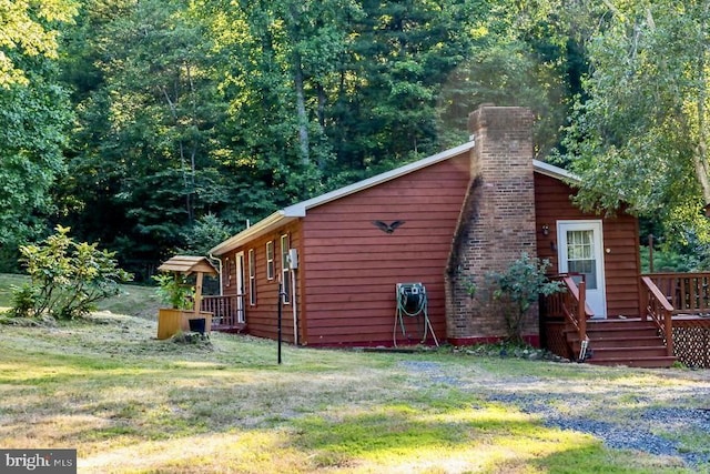 view of side of home featuring a chimney, a deck, and a lawn