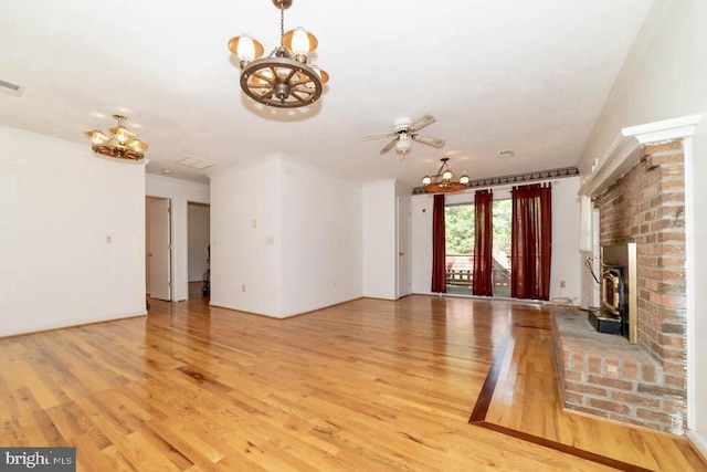 unfurnished living room featuring a chandelier, a brick fireplace, light wood-type flooring, and a ceiling fan