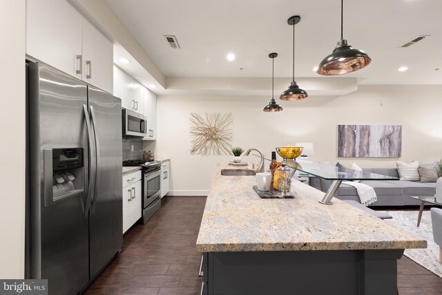 kitchen with appliances with stainless steel finishes, a sink, white cabinets, a center island with sink, and dark wood-style flooring