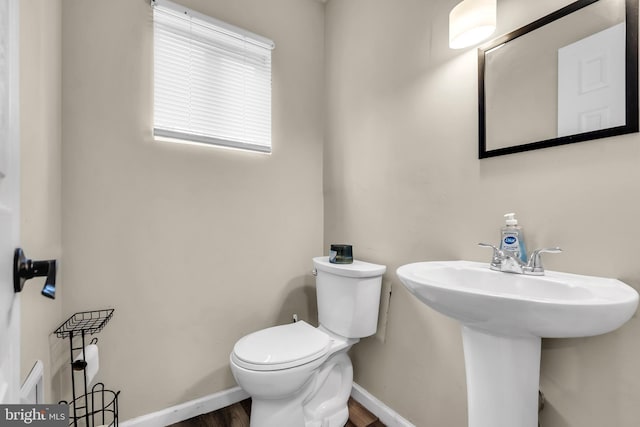 half bath featuring toilet, wood finished floors, baseboards, and a sink