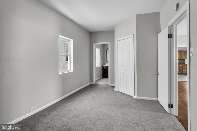 unfurnished bedroom featuring baseboards, carpet flooring, ensuite bathroom, and a closet
