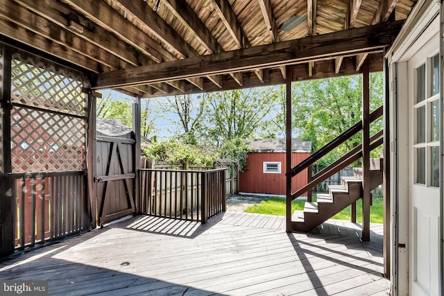 wooden deck featuring a storage unit, stairs, an outbuilding, and a fenced backyard
