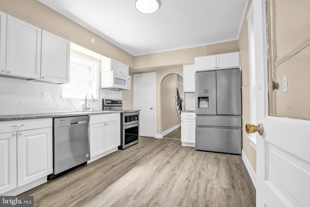 kitchen with appliances with stainless steel finishes, white cabinets, light wood-type flooring, a sink, and light stone counters