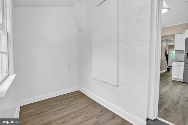 unfurnished dining area featuring baseboards, wood finished floors, arched walkways, and crown molding