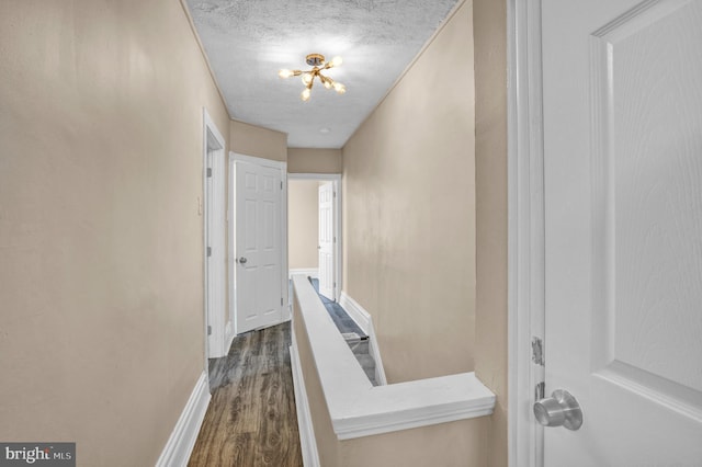 hall with dark wood-type flooring, baseboards, a textured ceiling, and a chandelier
