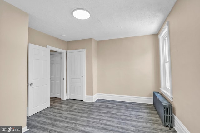 unfurnished bedroom featuring radiator, a textured ceiling, baseboards, and wood finished floors