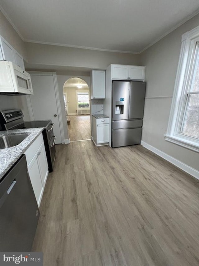 kitchen with stainless steel appliances, arched walkways, white cabinets, light stone counters, and crown molding