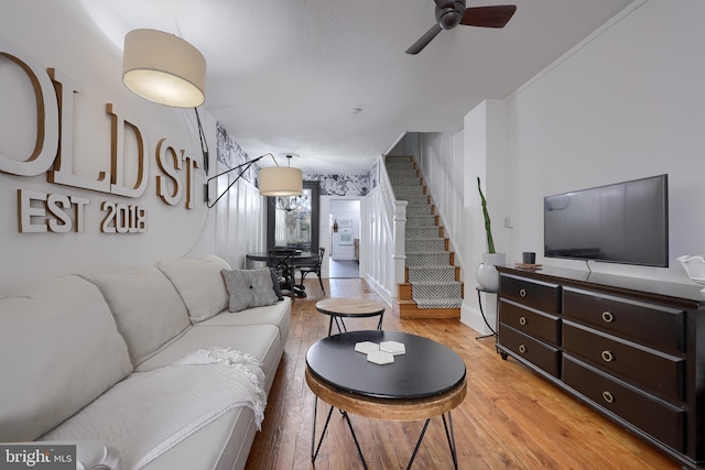 living area featuring stairway, light wood-type flooring, and a ceiling fan